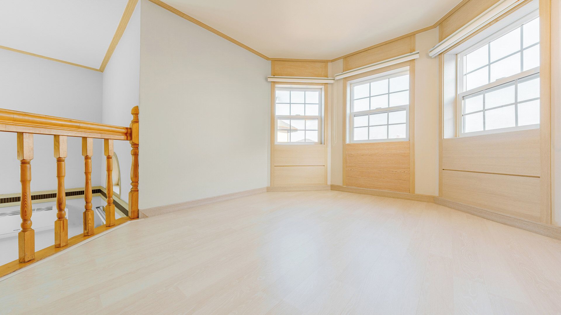 A spacious room with a wooden staircase, large windows, and a light-colored floor.