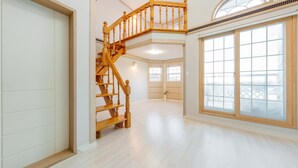 A spacious interior with a wooden staircase leading to an upper level, large windows with a view, and a clean, light-colored floor. - Geoje Peugeot Gomsol Petfriendly Pension (Geoje)