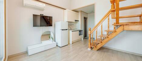 A modern kitchen with white appliances, a wooden staircase, and a flat-screen TV mounted on the wall.