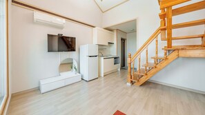 Une cuisine moderne avec des appareils électroménagers blancs, un escalier en bois et un téléviseur à écran plat fixé au mur.