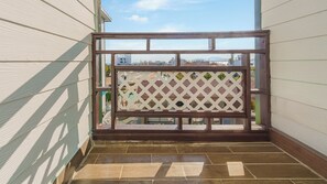 Un balcon doté d’une structure en bois et d’un treillis, offrant une vue sur les bâtiments et un ciel dégagé.