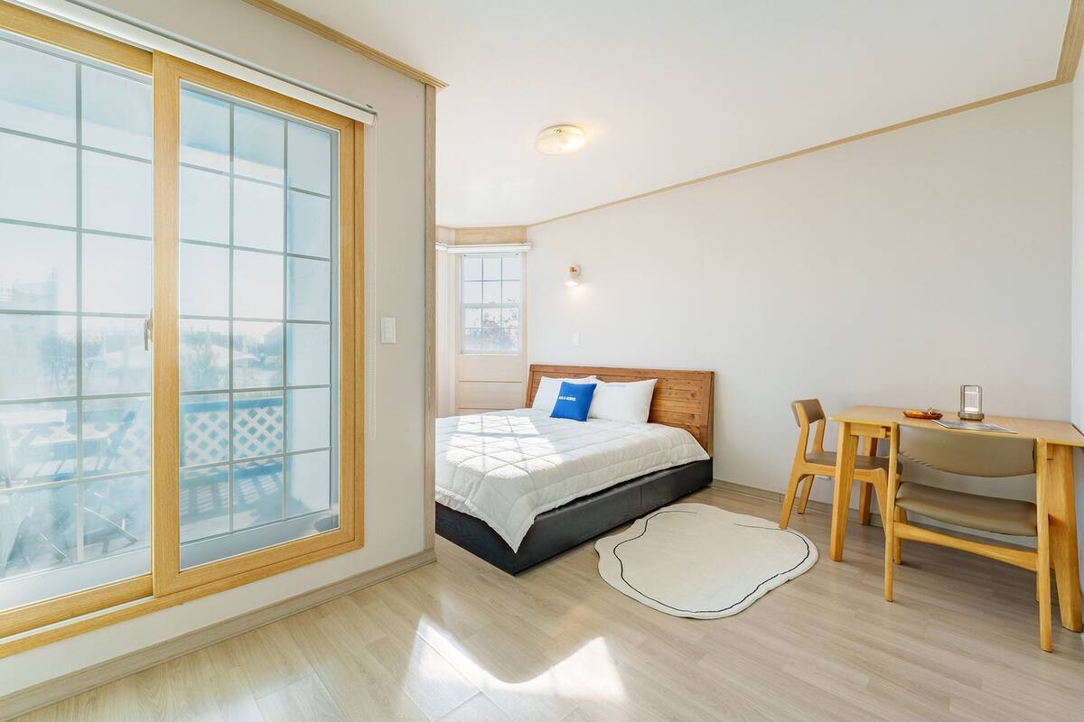 Ein Schlafzimmer mit Bett, Schreibtisch und einer großen SchiebeglasTür zum Außenbereich.