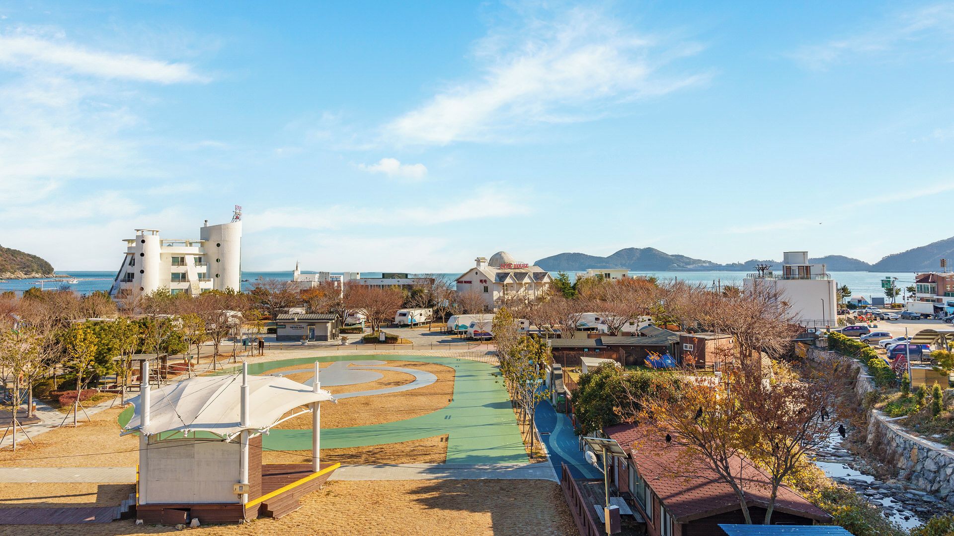 A coastal resort with a beach, a children's play area, and a view of the sea and mountains.