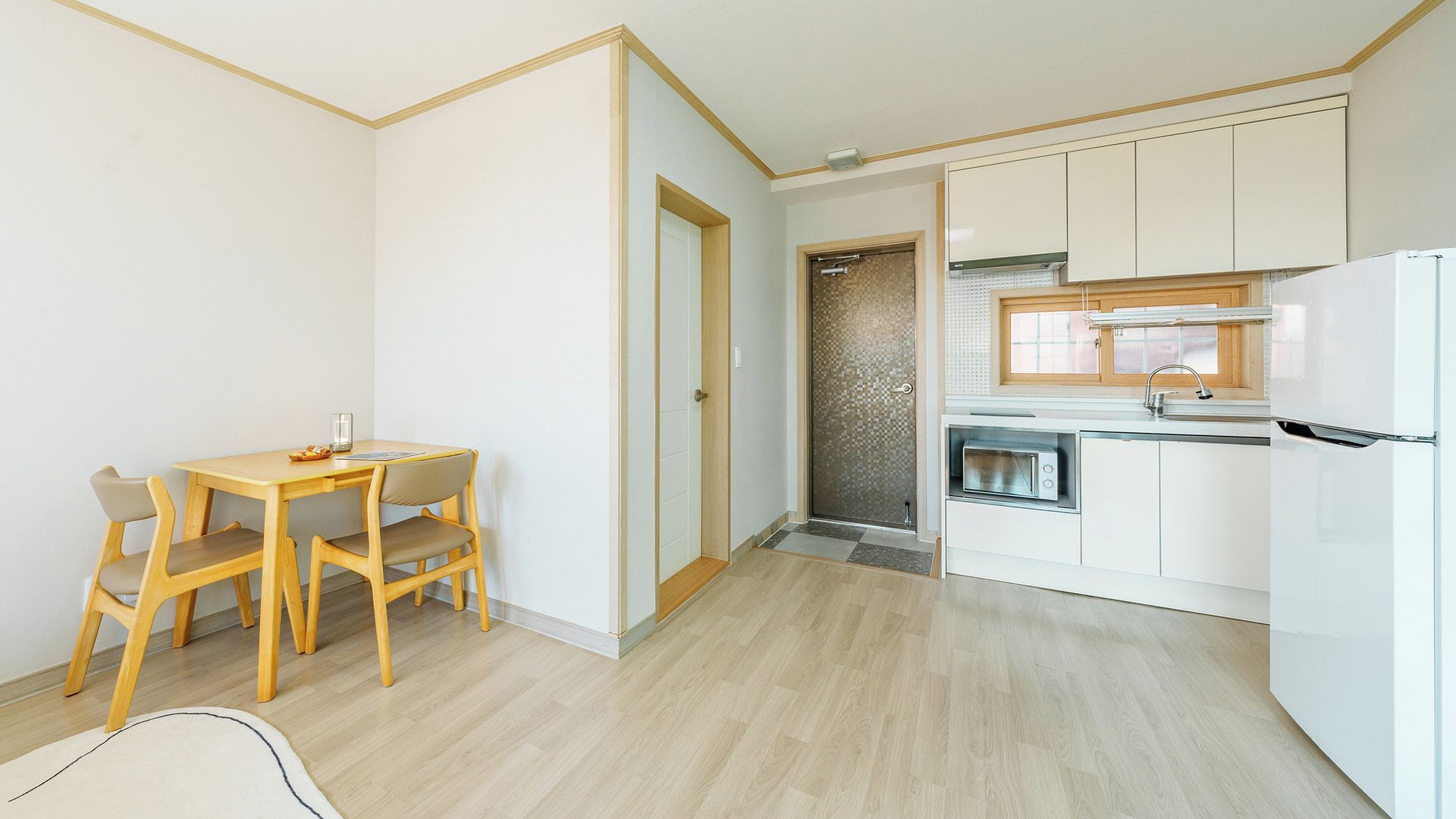 Cocina compacta con muebles blancos, horno empotrado y microondas.