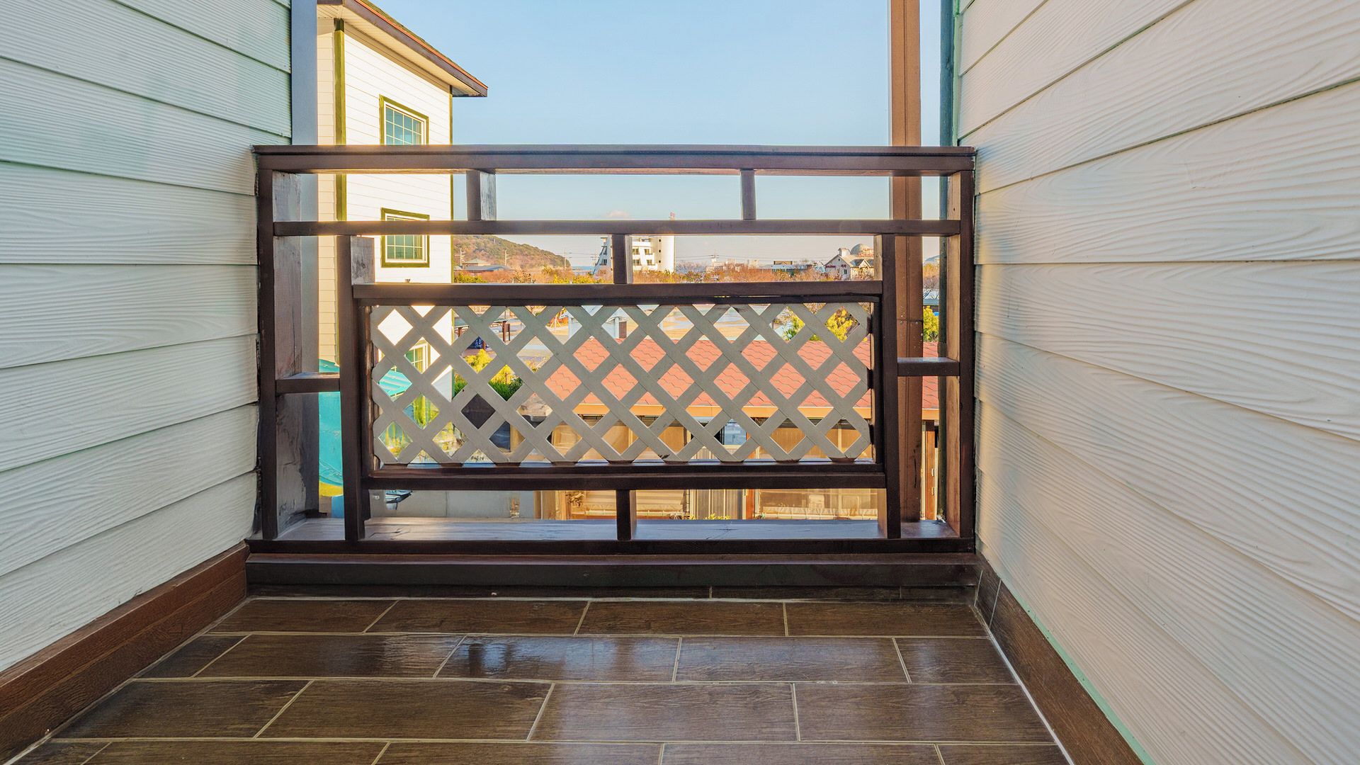 En balkon med trægulv, espalier og udsigt til bygninger i baggrunden.