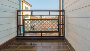 Un balcon doté d’un plancher en bois, d’une rambarde en treillis et offrant une vue sur les bâtiments qui se dressent à l’arrière-plan.