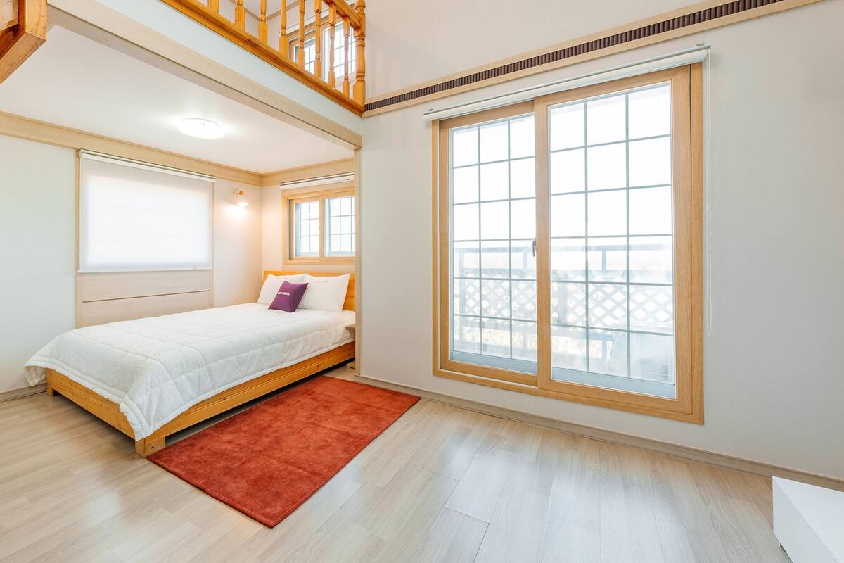 Ein Schlafzimmer mit einem Bett, einem großen Fenster und einer Treppe.