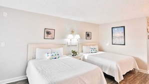 A hotel room with two beds, a nightstand with a lamp, and wall art.
