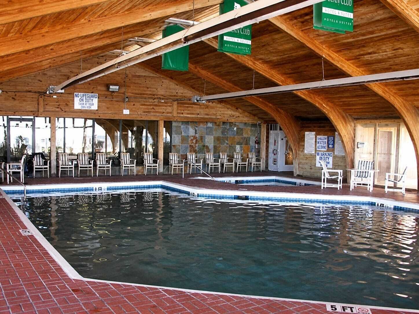 En inomhuspool med träbjälkar, solstolar och skyltar som visar att det inte finns någon badvakt i tjänst.