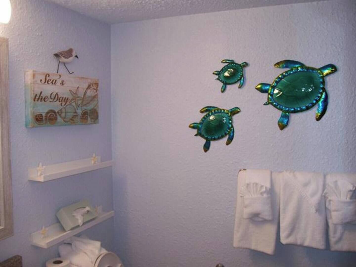 A bathroom with a light blue wall, a towel rack with white towels, and three sea turtle wall decorations.