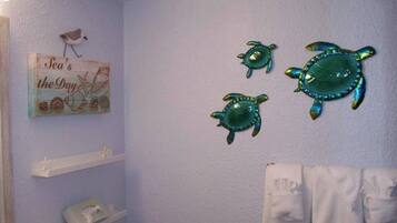 A bathroom with a light blue wall, a towel rack with white towels, and three sea turtle wall decorations.