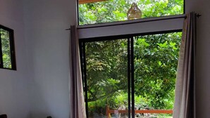 Une chambre avec un grand lit, une vue sur la verdure grâce à une porte-fenêtre coulissante et un plancher en bois.