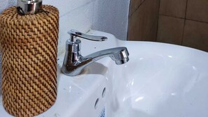 Une salle de bain avec un lavabo blanc, un robinet chromé et un distributeur de savon en osier.