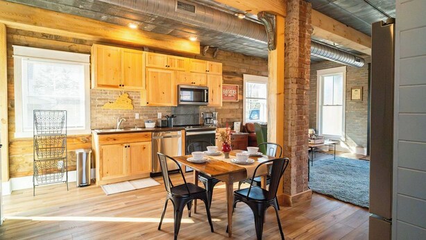 A rustic kitchen with wooden cabinets, a brick wall, and a dining area with a table and chairs.