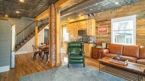 A spacious living area with a wooden floor, a green leather armchair, a brown leather sofa, and a dining table with chairs.