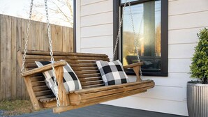 A wooden swing chair with checkered cushions, hanging from a chain, on a wooden deck.