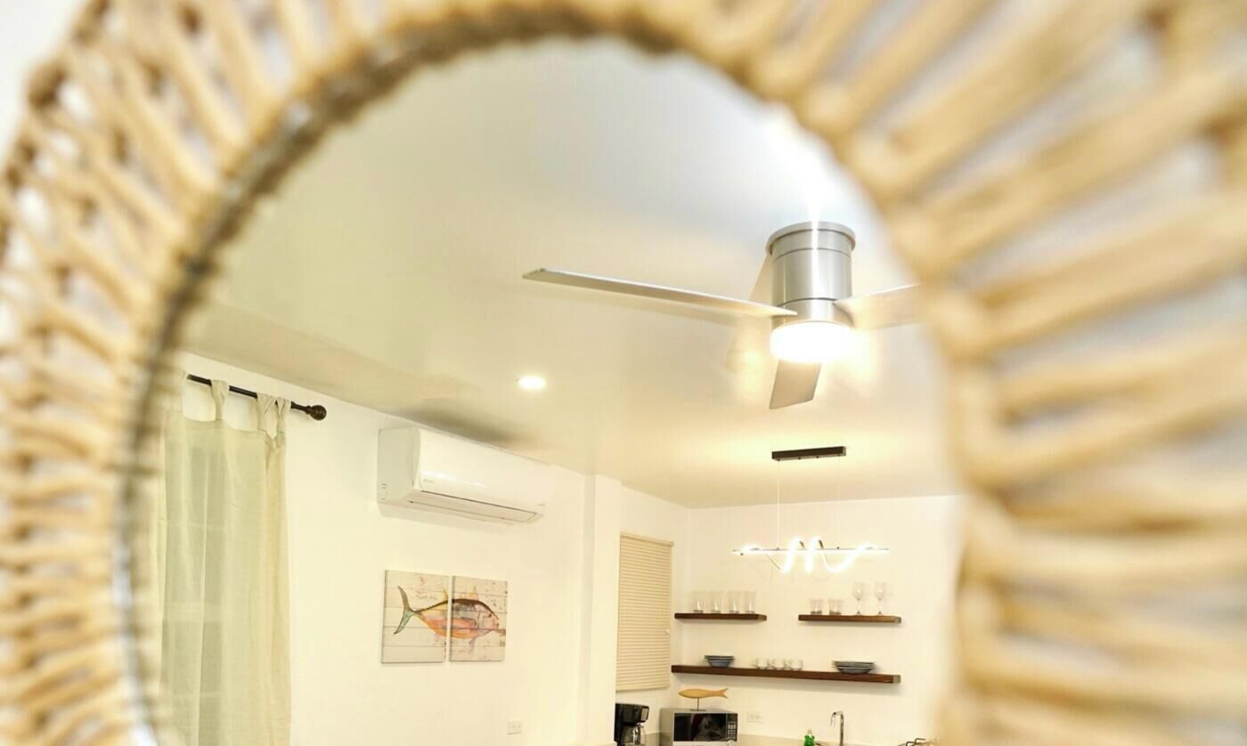 A modern kitchen with a ceiling fan, white walls, and a decorative mirror.