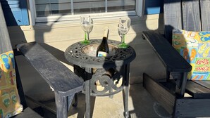 A patio with a round table, two chairs, and a bottle of wine. - Charming retreat across from Beach access 18 and steps to local attractions.  (Panama City Beach)