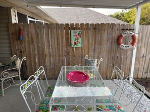 A glass-top table with chairs, a wooden fence, a beach-themed sign, and a lifebuoy. - Charming retreat across from Beach access 18 and steps to local attractions. (Panama City Beach)