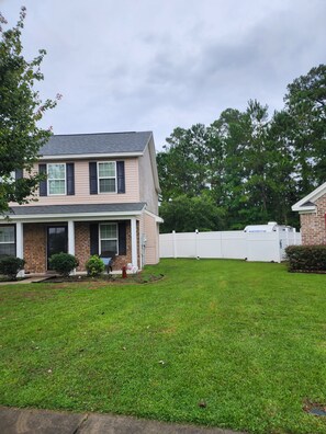 A two-story house with a front porch, a fenced backyard, and a brick exterior.
