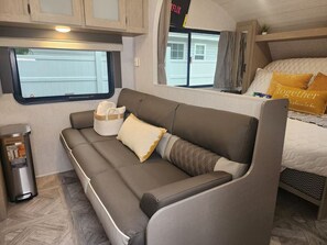 A cozy RV interior with a sofa, a trash can, and a bed with pillows.