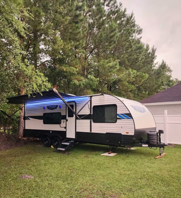 A mobile home with a blue awning, a sliding door, and a small attached utility vehicle.