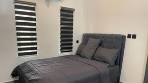 A bedroom with a bed, two windows with blinds, and a light switch on the wall. - Charming 2 bedroom apartment in nice area in  Lagos with WiFi, AC & security (Lagos)