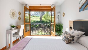 A bedroom with a large bed, a desk, and a balcony with a view of greenery. - Casa Valparón Porrúa Llanes - Terraces and Views (Porrua)