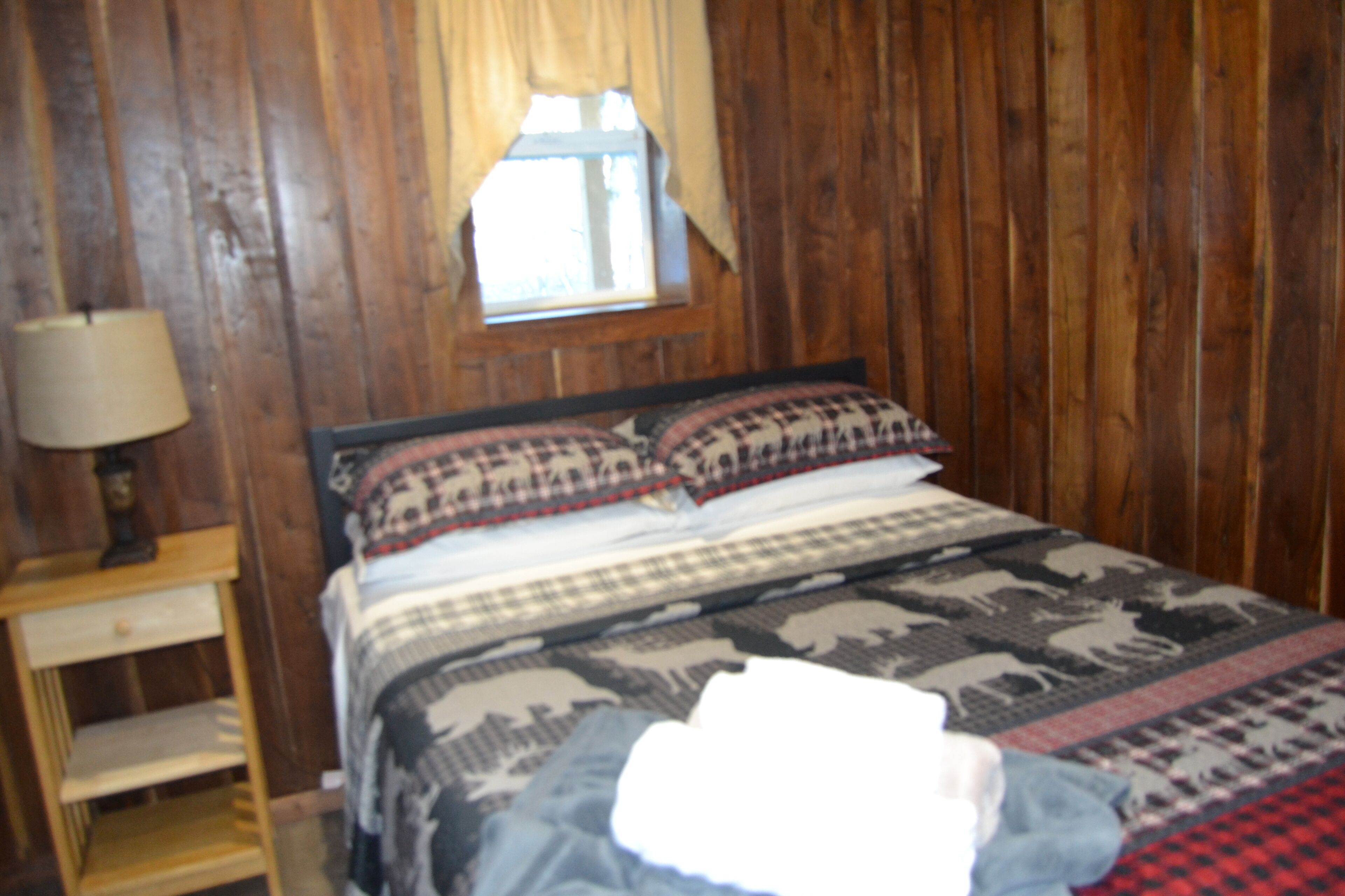 A wooden paneled room with a bed, a nightstand, and a window.