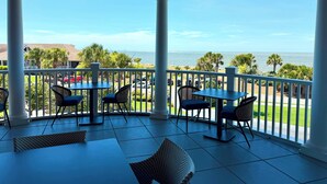 Ein überdachter Außenbereich mit Tischen und Stühlen, mit Blick auf Strand und Meer.