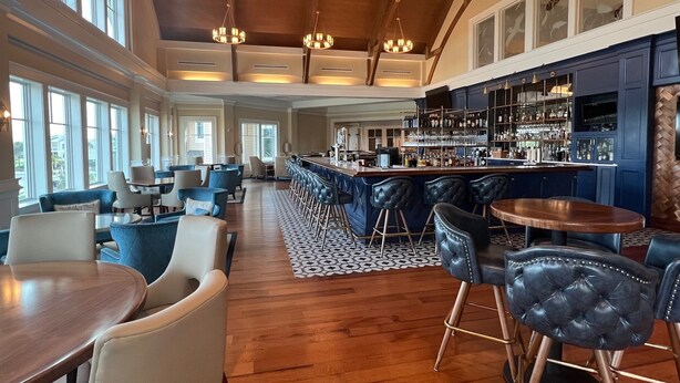 Eine großzügige Bar mit hohen Decken und großen Fenstern, inklusive einer Theke, Hockern und einer Lounge mit Tischen und Stühlen.