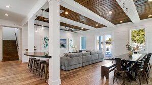 A spacious living area with a grey sofa, wooden flooring, and a dining area with a table and chairs. - 🌅 Saltwater Sunsets | Private Pool & Close to Beach | Dog Friendly* | FREE Excursions ☀️ (Destin)