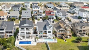 Uma área residencial costeira com várias casas de dois andares, uma piscina e uma praia ao fundo.