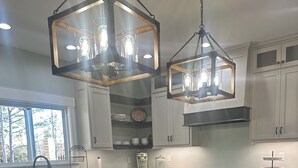 Una cocina moderna con una isla grande, un banco de madera, luces colgantes y armarios blancos.