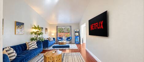 A living room with a blue sofa, a coffee table, and a Netflix sign on the wall.