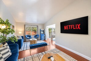 Un salon avec un canapé bleu, deux fauteuils, une table basse et un téléviseur fixé au mur sur le côté droit.