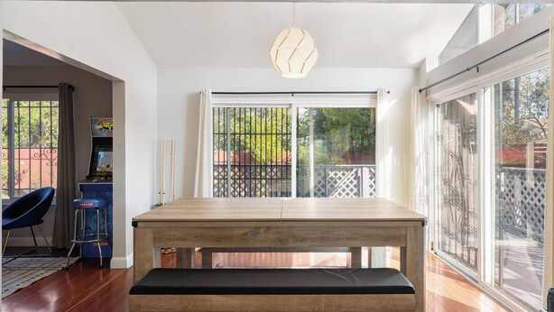 Een eethoek met een houten tafel en een bank, een blauwe stoel, en uitzicht door een groot raam.