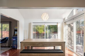 Un coin repas avec une table et un banc en bois, une chaise bleue et une vue sur l’extérieur par le biais d’une grande fenêtre.