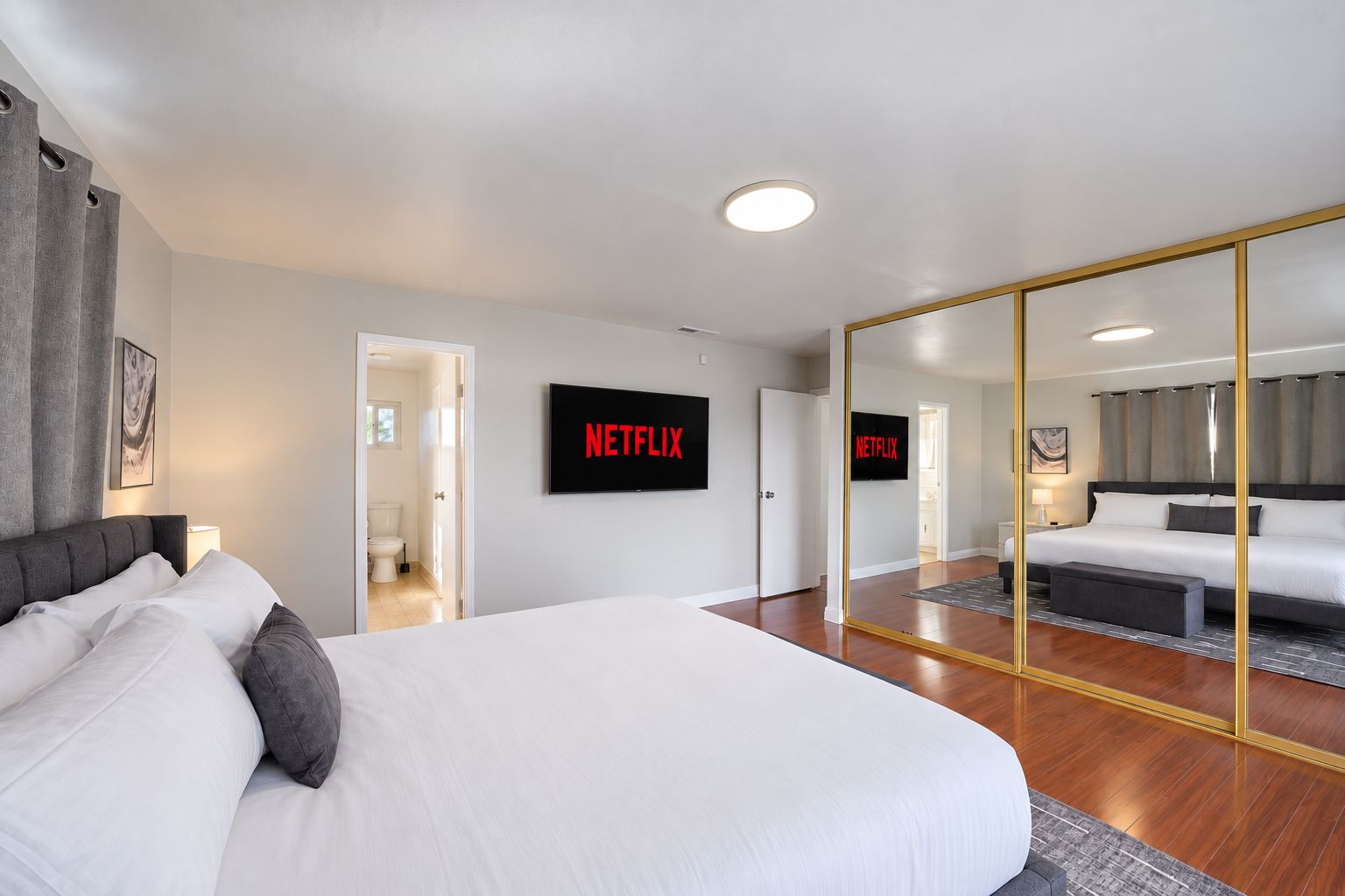 Moderni hotellihuone, jossa on suuri sänky, seinälle asennettu taulutelevisio ja suuri peili, joka heijastaa huonetta.