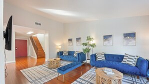 Een moderne woonkamer met een blauwe zithoek, een houten salontafel en een vloerkleed met een patroon.