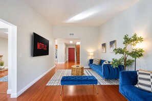 Un salon moderne avec un téléviseur à écran plat, un canapé bleu, une table basse et une plante en pot.
