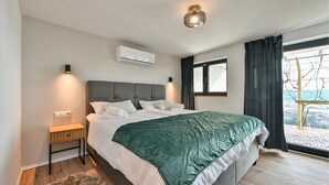A modern bedroom with a large bed, a nightstand, an air conditioning unit, and a view of the outdoors. - 1 bedroom beautiful home in Remetinec (Remetinec)