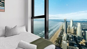 Une chambre avec une grande fenêtre donnant sur une plage et sur le paysage urbain.