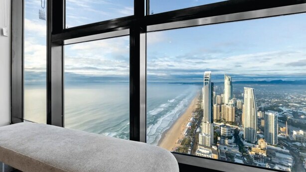 Une chambre située dans un immeuble de grande hauteur, dotée d’une grande fenêtre donnant sur une plage et le panorama urbain.