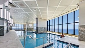 Une piscine intérieure offrant une vue dégagée sur l’océan, un sol carrelé et un design de plafond moderne.