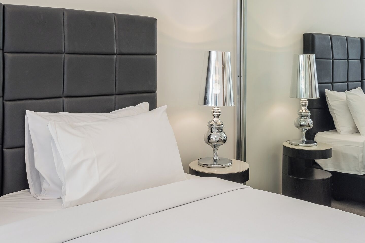 A modern hotel room with a large bed, two bedside tables, and a mirror.