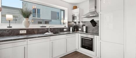 A modern kitchen with white cabinets, a large window, a built-in oven, and a coffee maker.