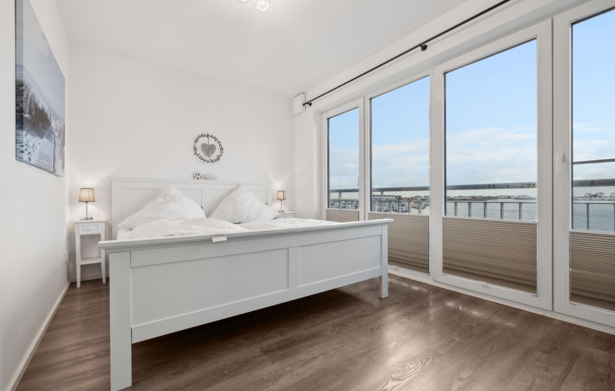 Une chambre avec un grand lit, une table de chevet, un décor mural en forme de cœur et une vue sur un pont et l’eau, visible à travers de grandes fenêtres.