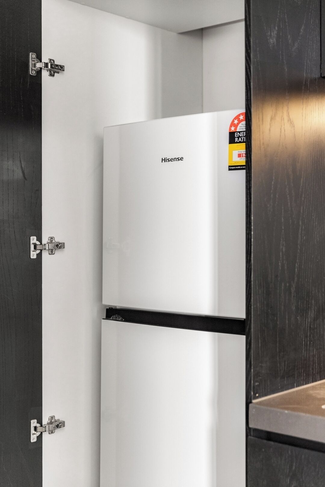 Un refrigerador blanco de Hisense en una cocina con armarios de madera oscura y un protector contra salpicaduras de acero inoxidable.
