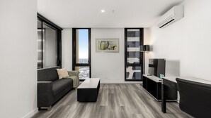 A modern living room with a grey sofa, a coffee table, a TV, and a city view through large windows.